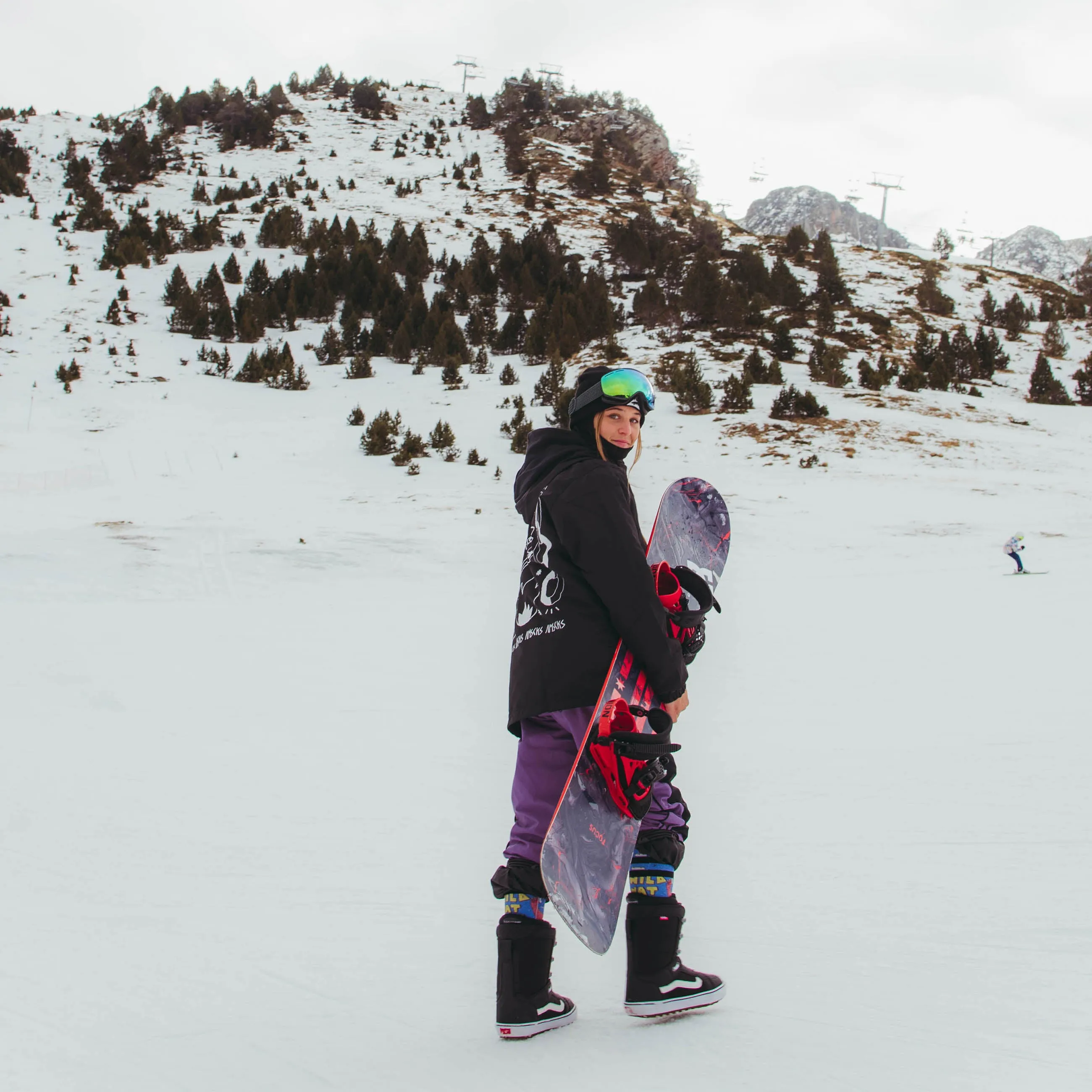 Snowboarder con lo snowboard davanti a un paesaggio montano innevato, con indosso le calze Wild Nature Snow Socks.