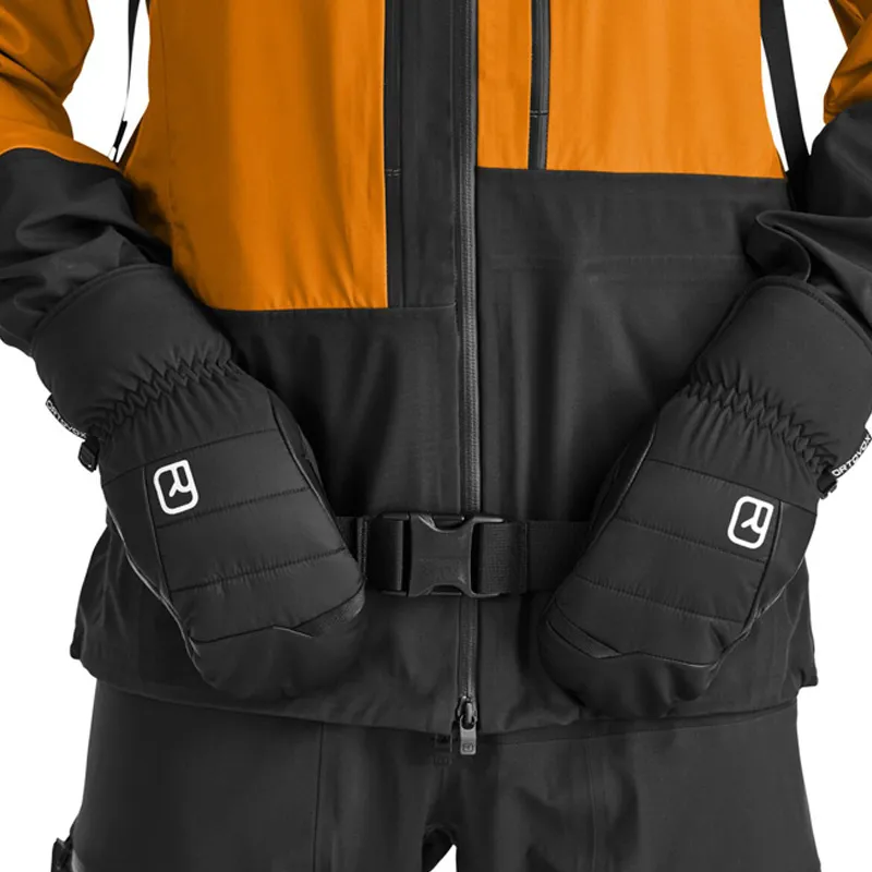 Primo piano: guanti neri Ortovox Freeride Cozy davanti a una giacca invernale con cintura.