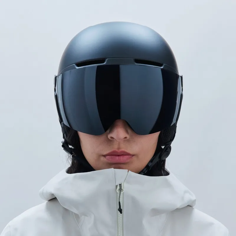 Eine Person trägt einen schwarzen Skihelm mit Visier. Das Visier ist dunkel getönt. Die Person trägt eine weiße Jacke mit Reißverschluss.