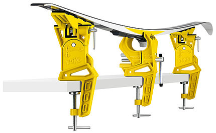 Gelb-silberne Toko Ski Vise Worldcup Adapter-Halterung mit Ski, an einer weißen Oberfläche befestigt.