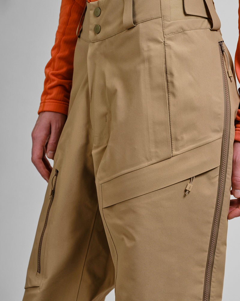 Y-1 HD GORE-TEX Hose Detailaufnahme der sandfarbenen Y-1 HD GORE-TEX Pro Shell Hose mit Taschen und Reißverschlüssen, getragen von einer Person.