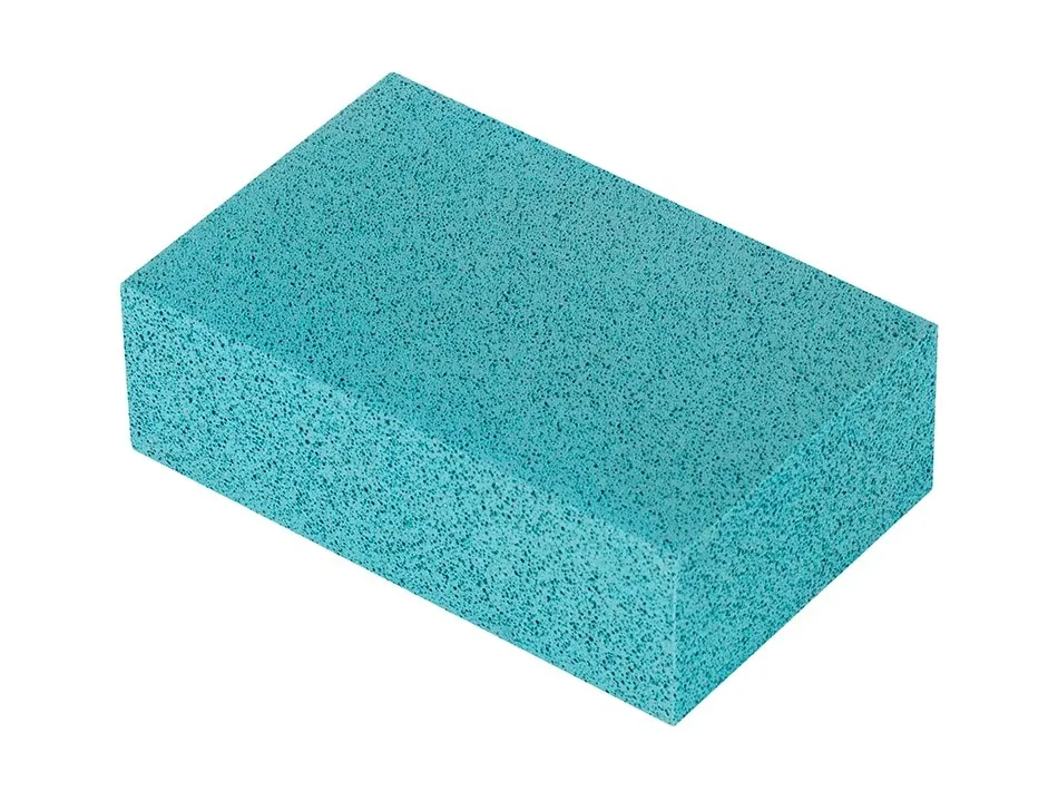 Una pietra pomice rettangolare di colore turchese chiaro è isolata su uno sfondo bianco. La sua superficie appare porosa.