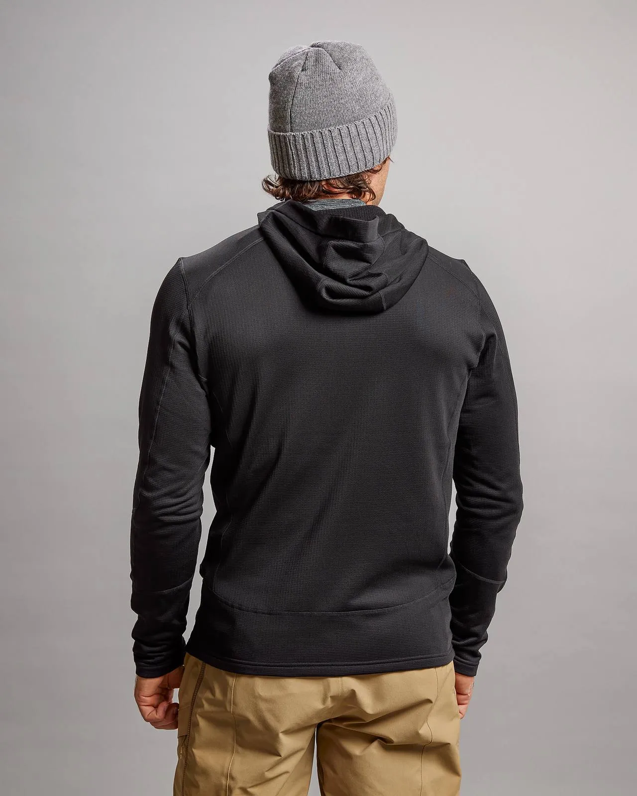 Back view of a black M-4 Techno Stretch Mid Hood jacket with hood, combined with a gray cap and beige pants.