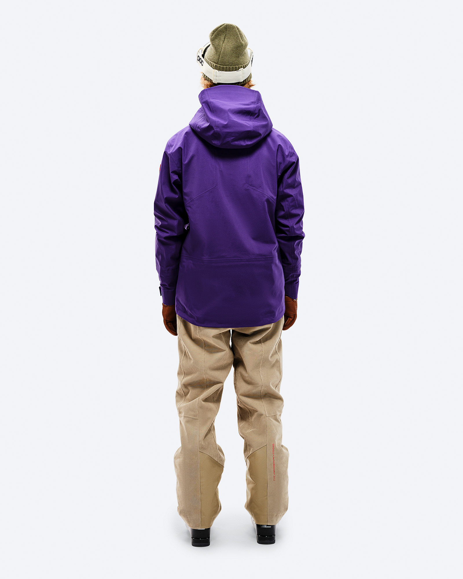 Veste GORE-TEX violette Personne de dos en veste GORE-TEX Shell violette, pantalon beige, casquette et lunettes de ski.
