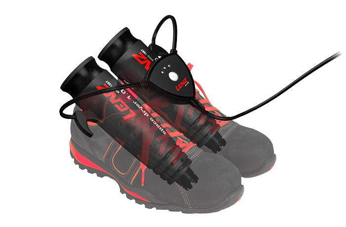 Zwei Arbeitsschuhe mit Schuhtrockner, der in die Schuhe gesteckt ist und mit einem Bedienfeld verbunden ist. Schwarzes Kabel führt weg.
