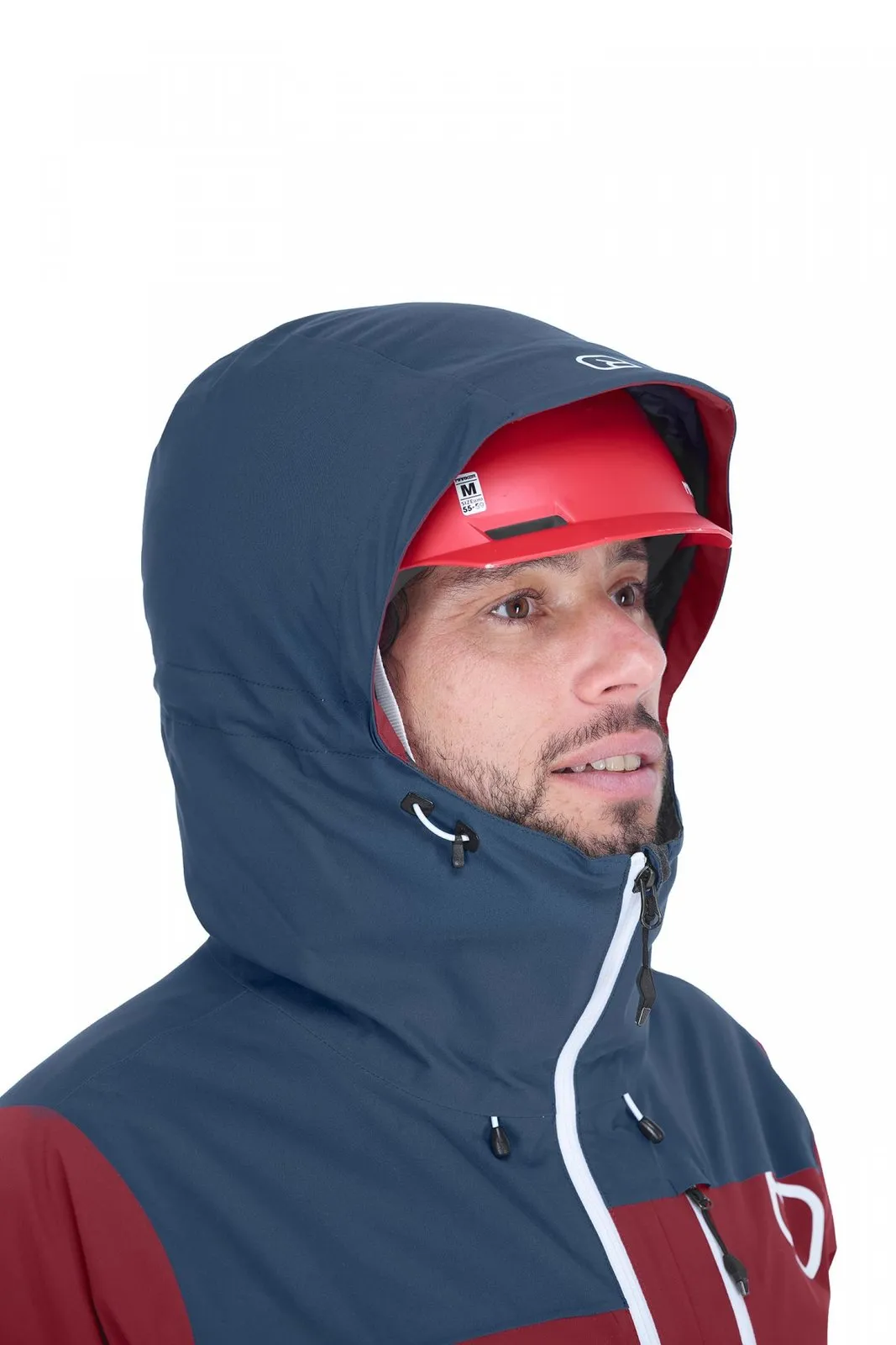 Man with red helmet wearing the blue Ortovox Andermatt jacket with hood, which partially covers his face.