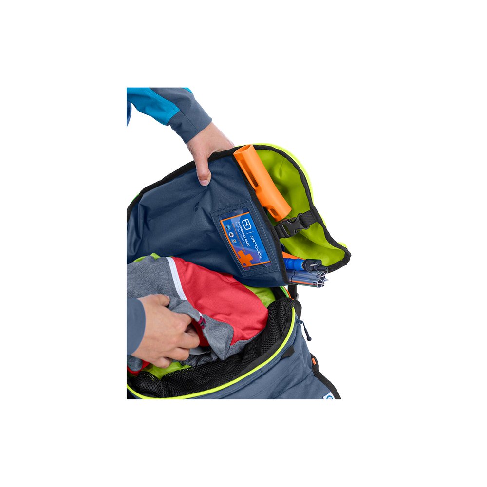 Sac à dos Cross Rider 18 ouvert, rempli de vêtements et d'équipement d'avalanche, la main saisit l'intérieur.