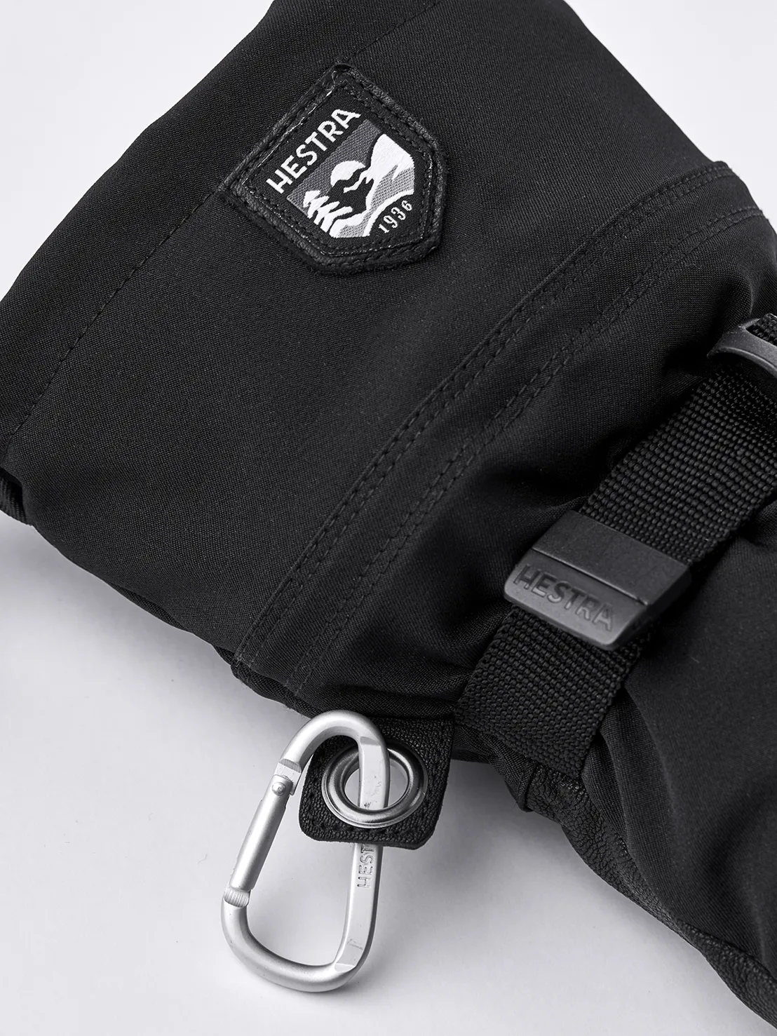 Gros plan sur une mitaine noire Hestra Army Leather Extreme Mitt avec mousqueton et logo.