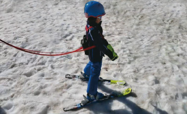 Ski Trainer enfant Enfant avec entraîneur de ski sur la neige. L'enfant porte un casque bleu et est guidé par des laisses.