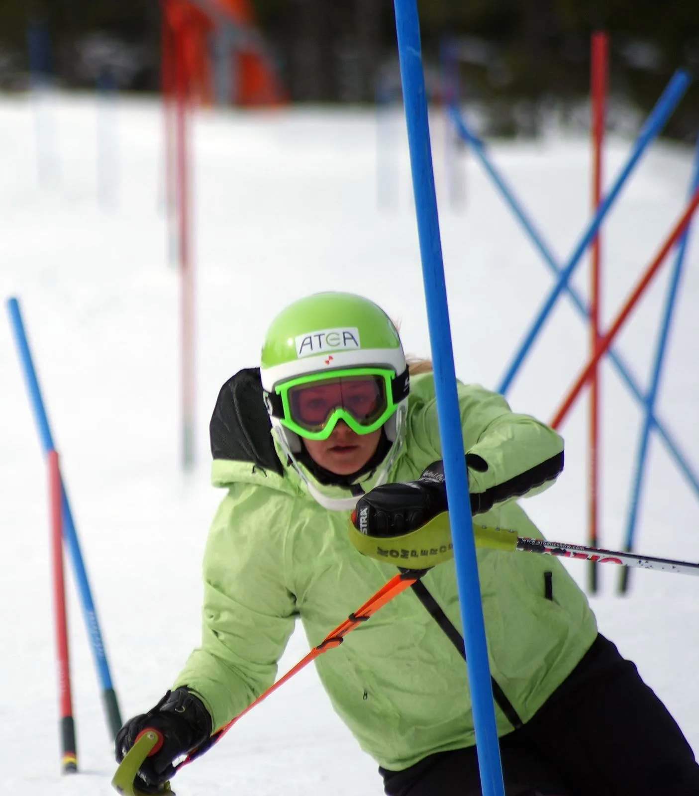 Skier with training strap between poles. Ski helmet and goggles in green, orange strap.
