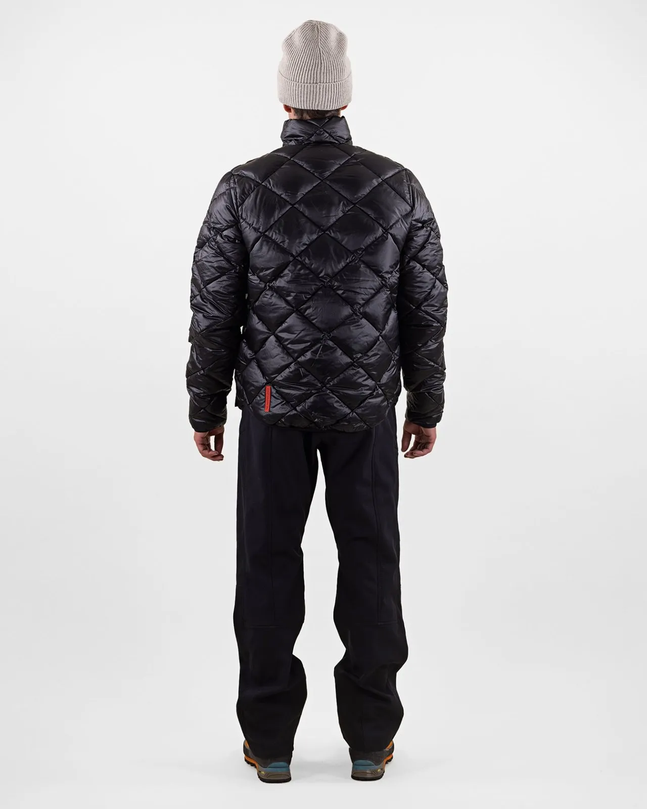 Person von hinten, trägt schwarze Daunenjacke mit Rautenmuster, Hose und Mütze.