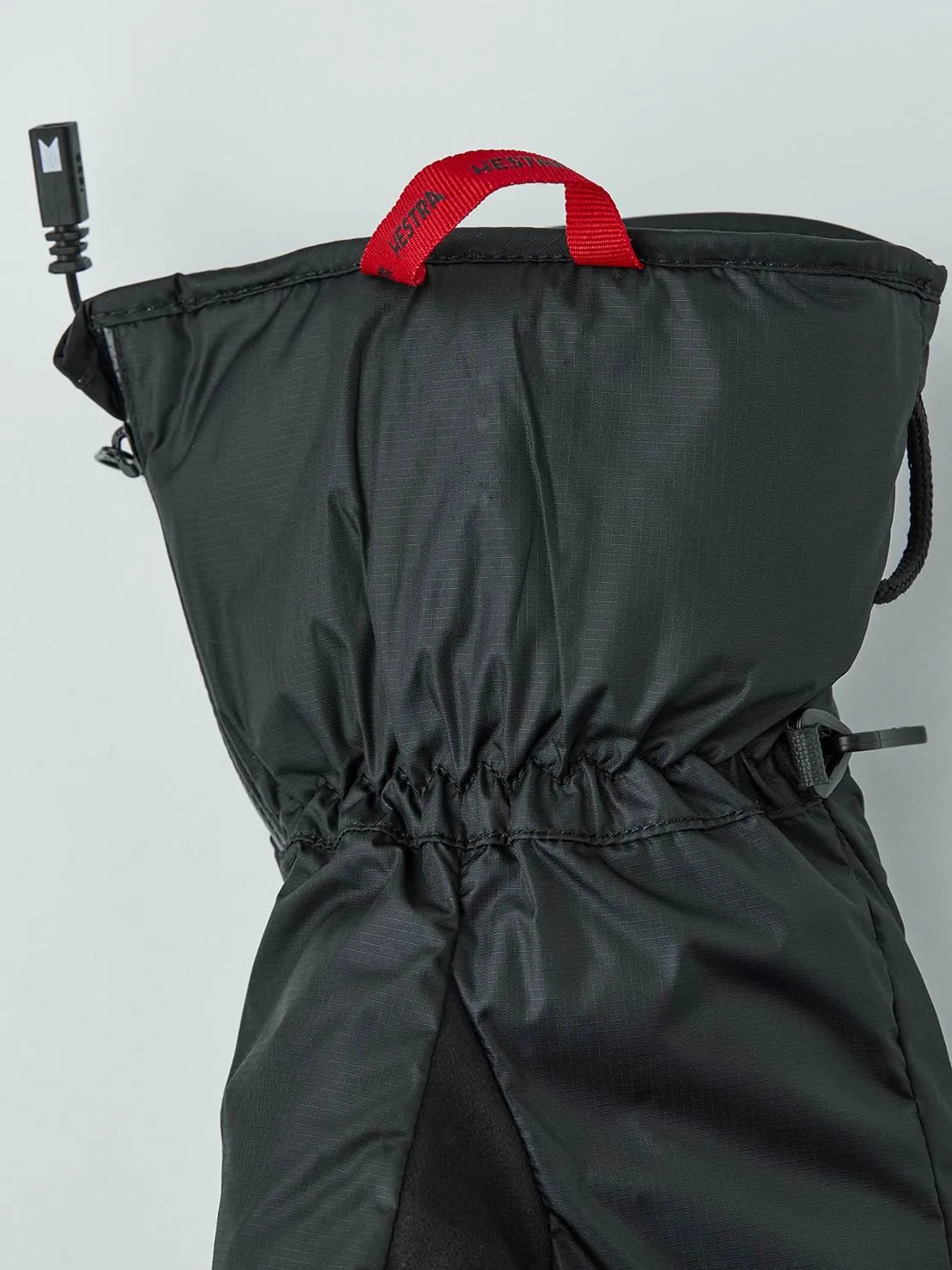 Black heatable inner glove with red Hestra loop, drawstring and connection cable against a neutral background.