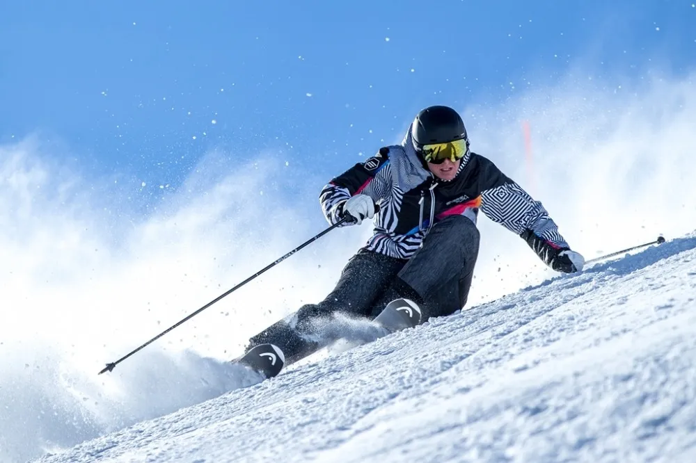 Skifahrer in "Jeans Optical" Hose fährt auf einer schneebedeckten Piste, Spritzender Schnee umgibt ihn.