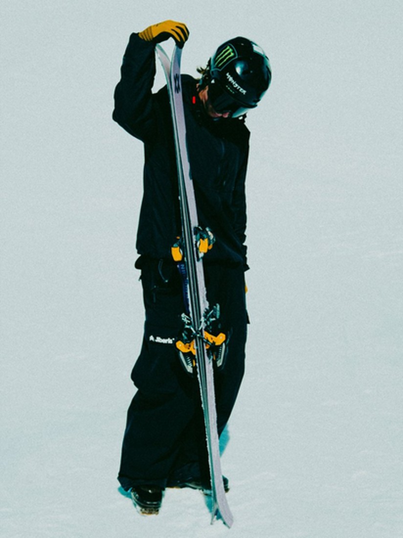Skifahrer mit Skiern Skifahrer in dunkler Kleidung und Helm mit Skiern. Er trägt gelbe Handschuhe.