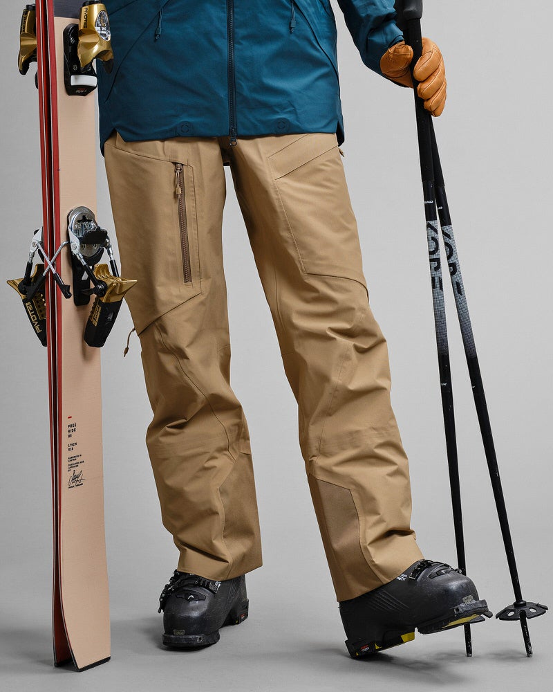 Skifahrer in GORE-TEX Hose Person mit Skiern und Stöcken, bekleidet mit Sandfarbener GORE-TEX Pro 3L Shell Pant und Skischuhen.