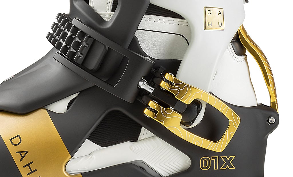 Dahu Ecorce 01X Skischuh Nahaufnahme des Dahu Ecorce 01X Skischuhs in Weiß, Schwarz und Gold. Details der Schnalle und des Logos sind sichtbar.