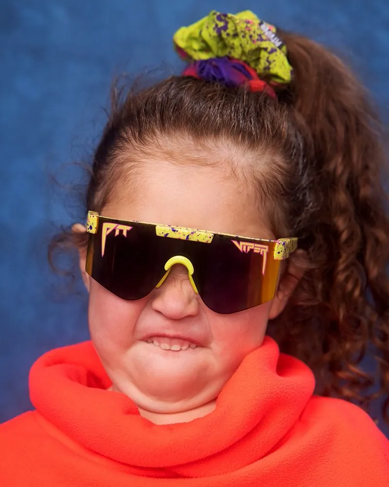 Bambino con occhiali da sole "The 1993 XS" a macchie gialle e maglione rosso fa una smorfia.