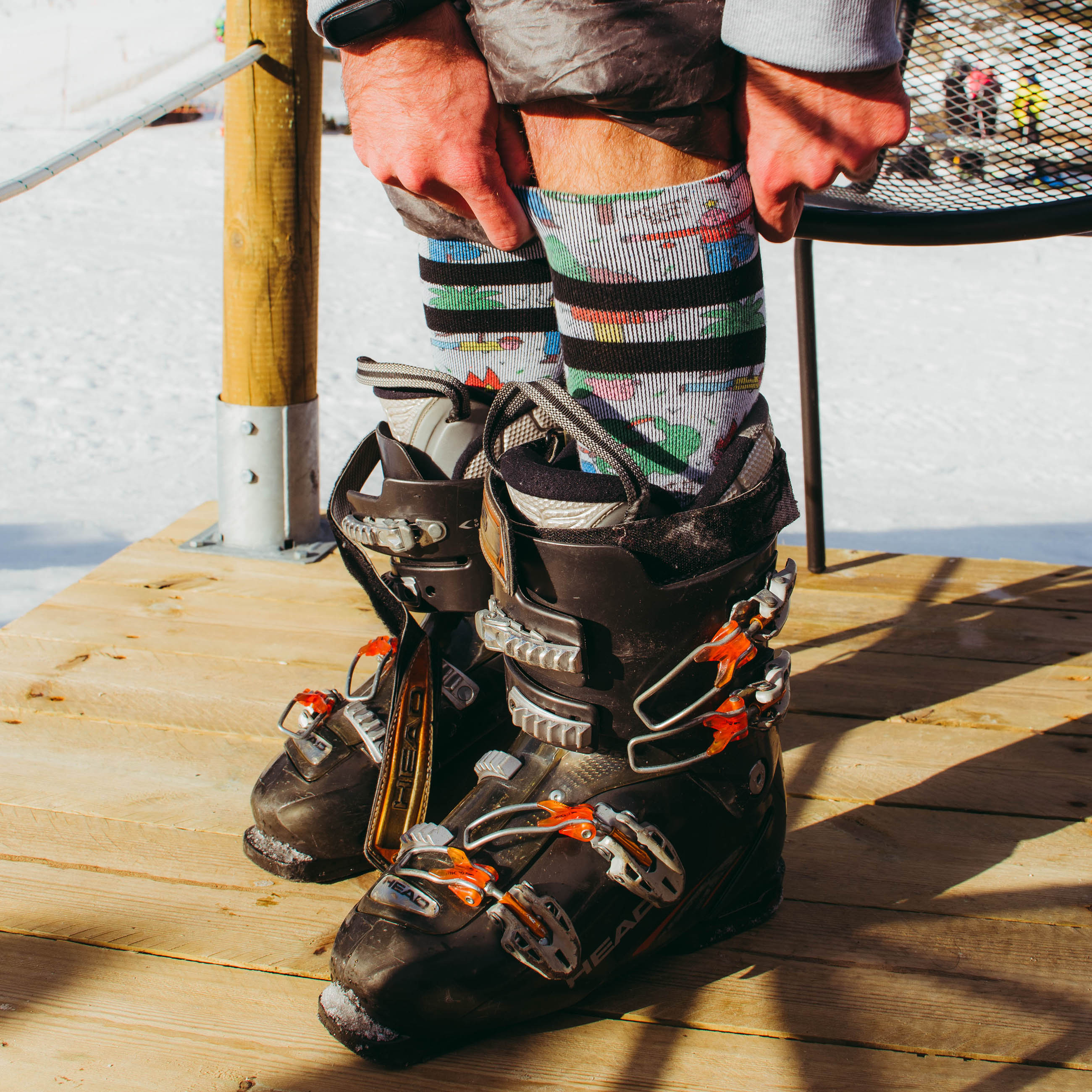 Bunte Snow Socks Nahaufnahme von Snow Socks mit buntem Muster und Skischuhen auf Holzbrett im Schnee.