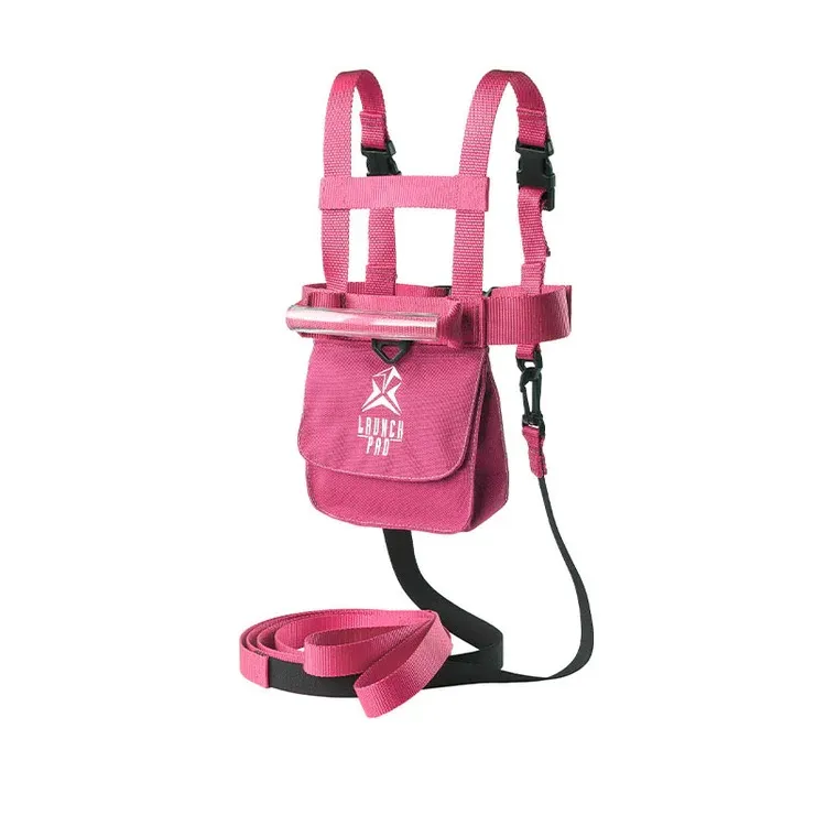 Pink ski harness for toddlers with a handle and removable leash. Adjustable shoulder and waist straps, front pocket with 'LAUNCH PRO' logo, and black buckles. Leash is coiled for added safety.