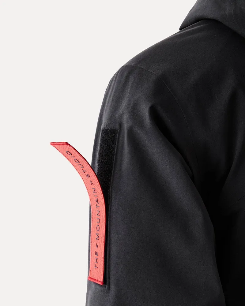 Detailaufnahme einer schwarzen Gore-Tex S-1 Jacke; Ärmel mit rotem Band mit Aufschrift "The Mountain Studio".