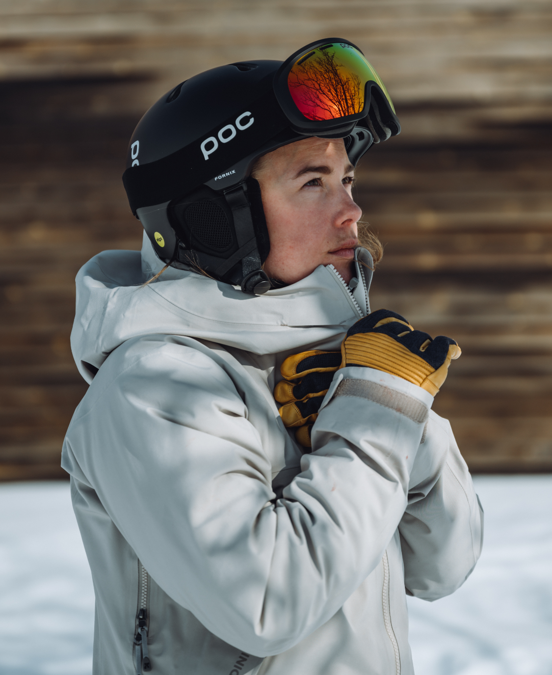 Skifahrer mit Helm Person mit Poc Fornix Mips Skihelm und Skibrille blickt nach links; reflektierende Bäume in der Brille.
