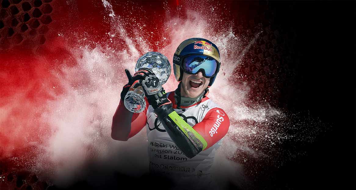 Ein Skirennläufer mit Helm und Skibrille hält einen Kristallpokal in die Höhe.