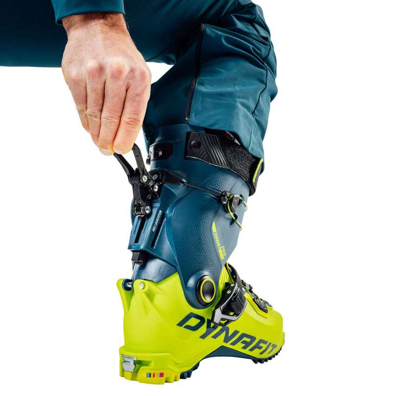 Ein Dynafit Radical Pro Tourenskischuh wird von einer Hand bedient, Hoji Lock-System ist sichtbar, Farbe ist Gelb/Blau.