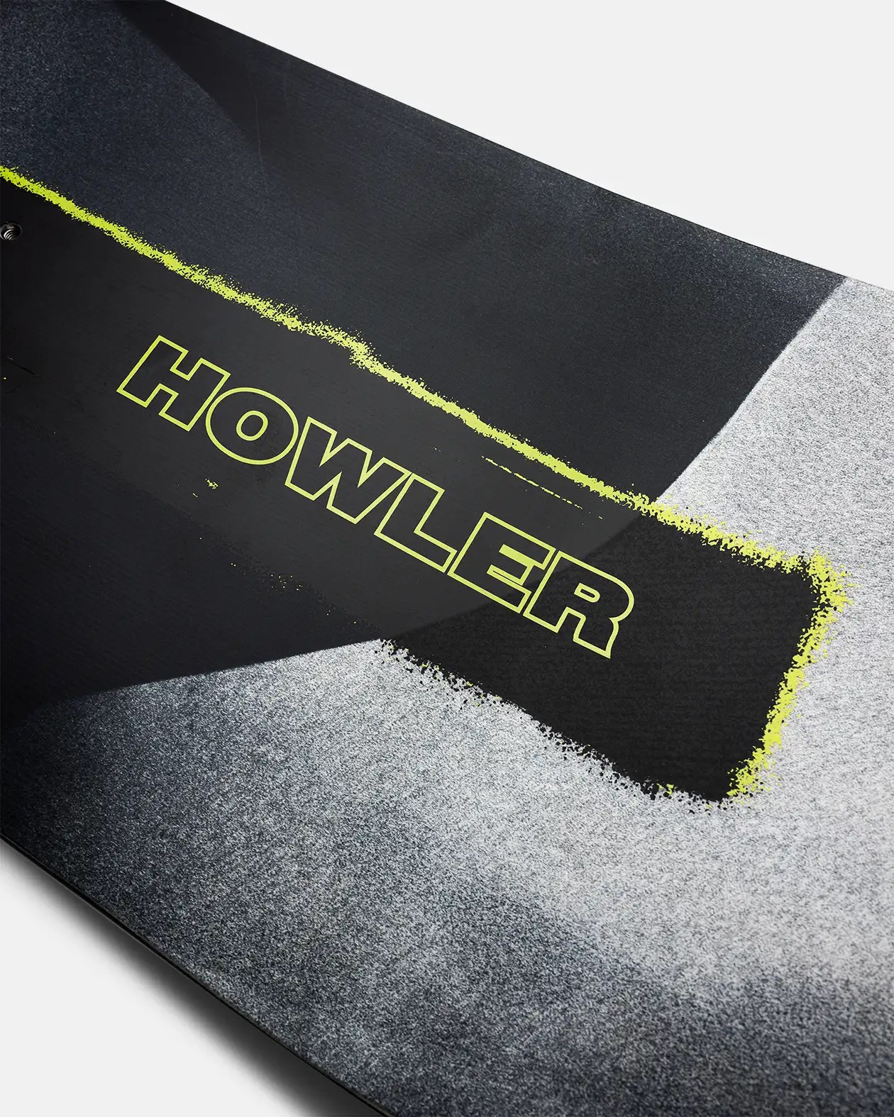 Detailansicht eines Snowboards mit grauen Sprühfarbeffekt und dem neon-gelben Schriftzug "HOWLER" auf einem schwarzen Rechteck.