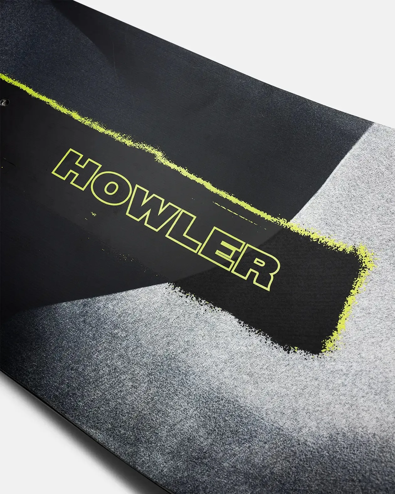 Vista dettagliata di uno snowboard con effetto vernice spray grigia e la scritta "HOWLER" in giallo neon su un rettangolo nero.