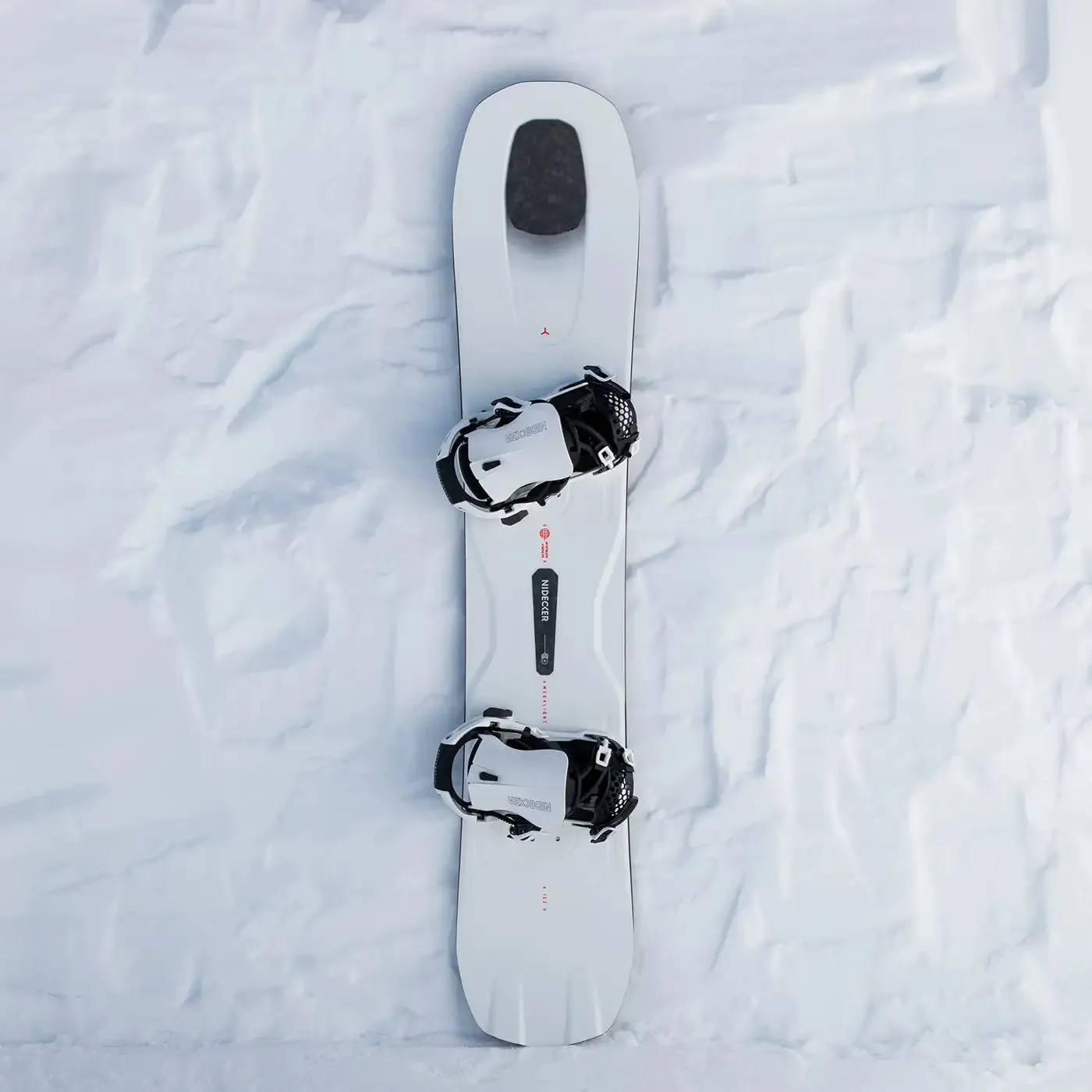 Weisses Snowboard mit Bindungen liegt flach auf Schnee, von oben betrachtet.