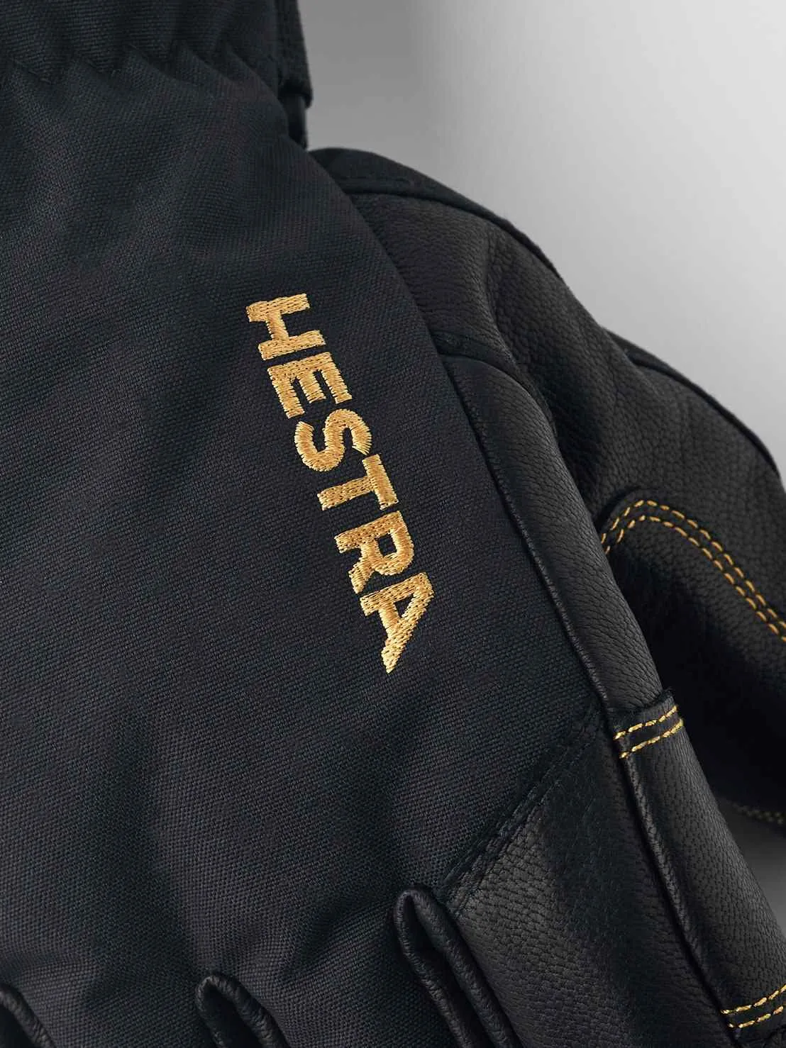 Close-up of a black Hestra Gore-Tex five-finger glove with gold-colored Hestra logo.
