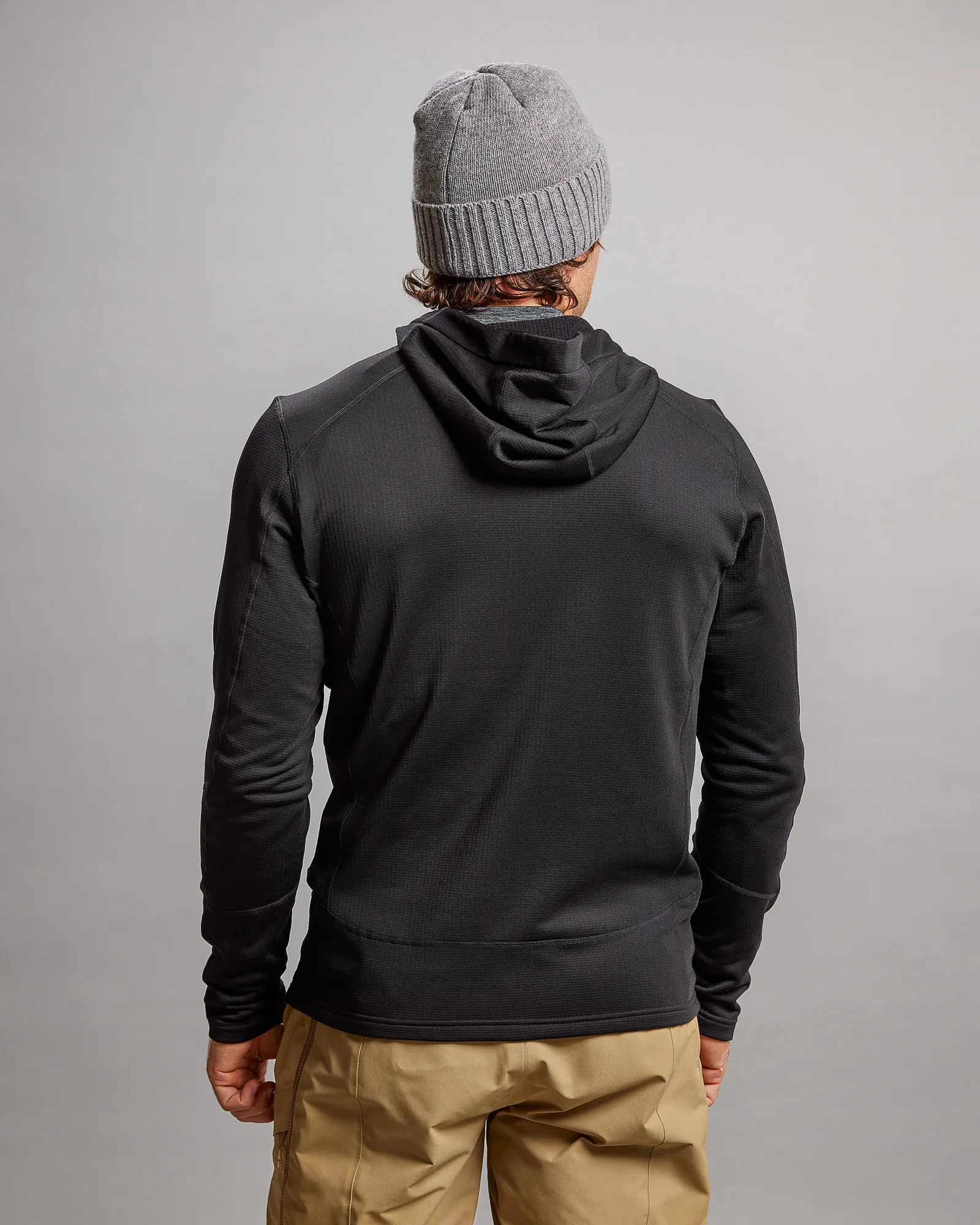 Vue arrière d'une veste noire M-4 Techno Stretch Mid Hood avec capuche, combinée avec une casquette grise et un pantalon beige.