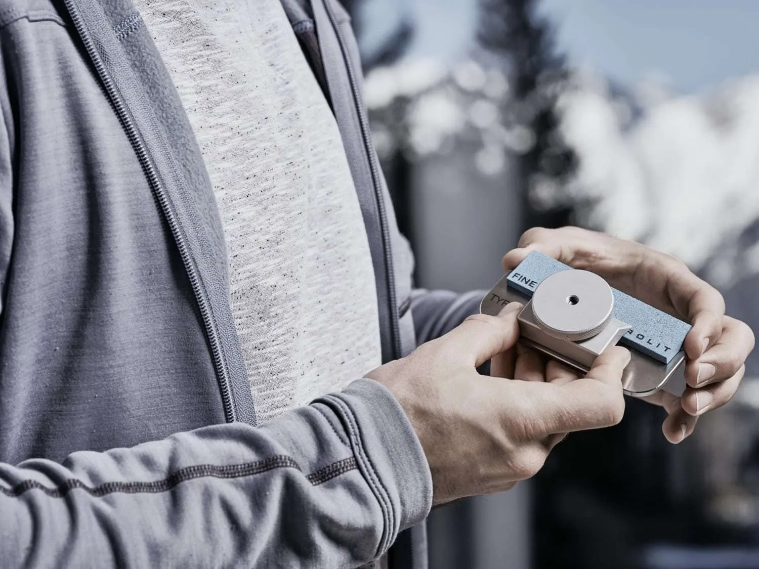 A person holds a Tyrolit sharpener with the inscription "FINE" and "Tyrolit" in front of a blurred mountain backdrop.