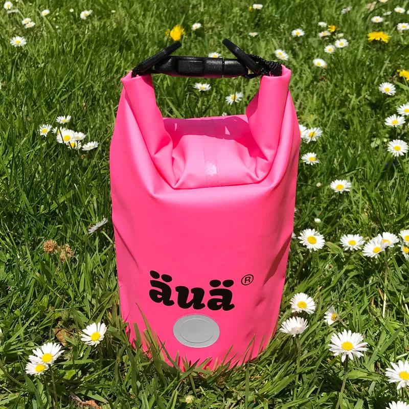 Pinker wasserdichter Packsack der Marke äuaä, platziert im grünen Gras mit Gänseblümchen.