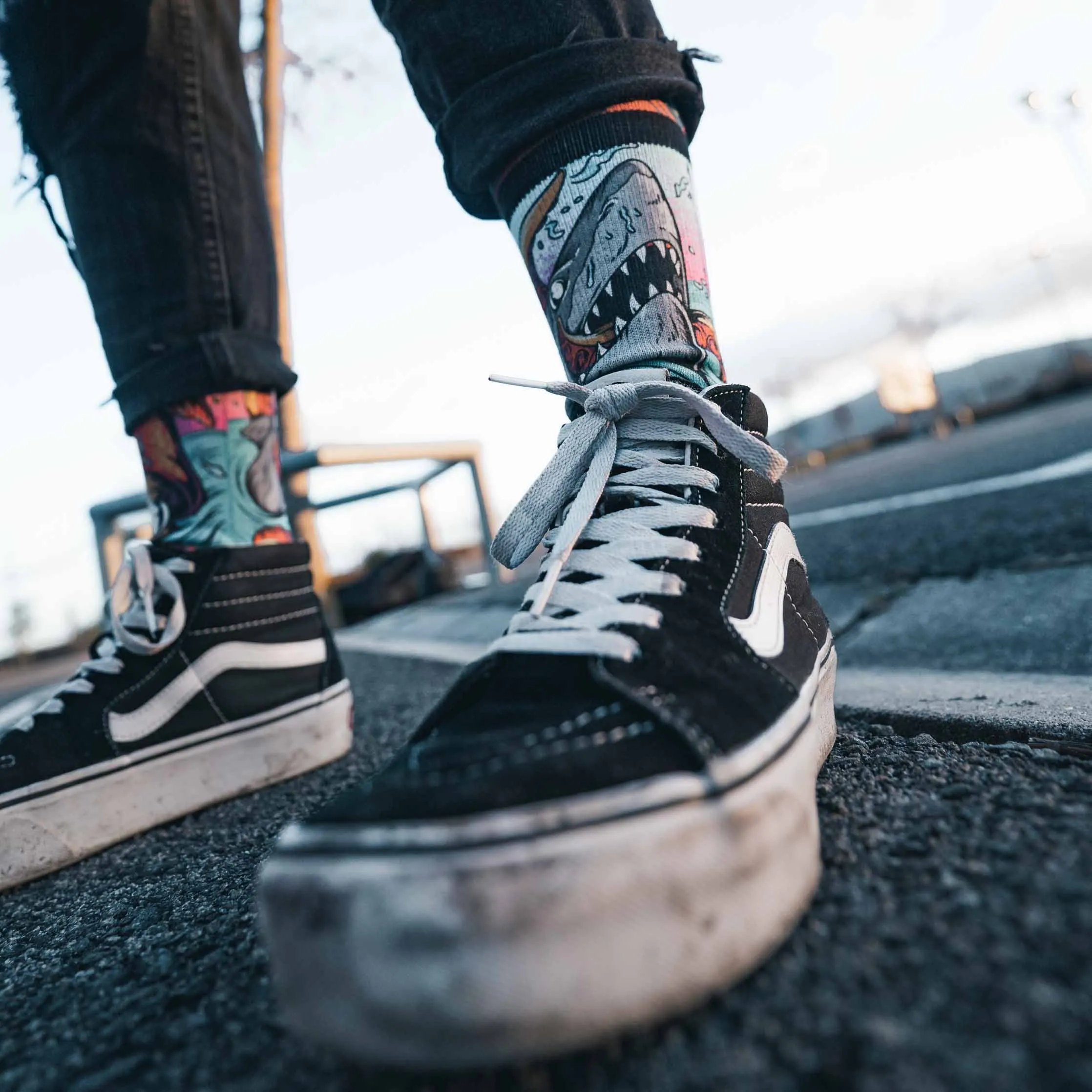 Person mit schwarzen Jeans und schwarzen Schuhen trägt "Seamonsters - Mid High" Socken mit Haifischmuster.