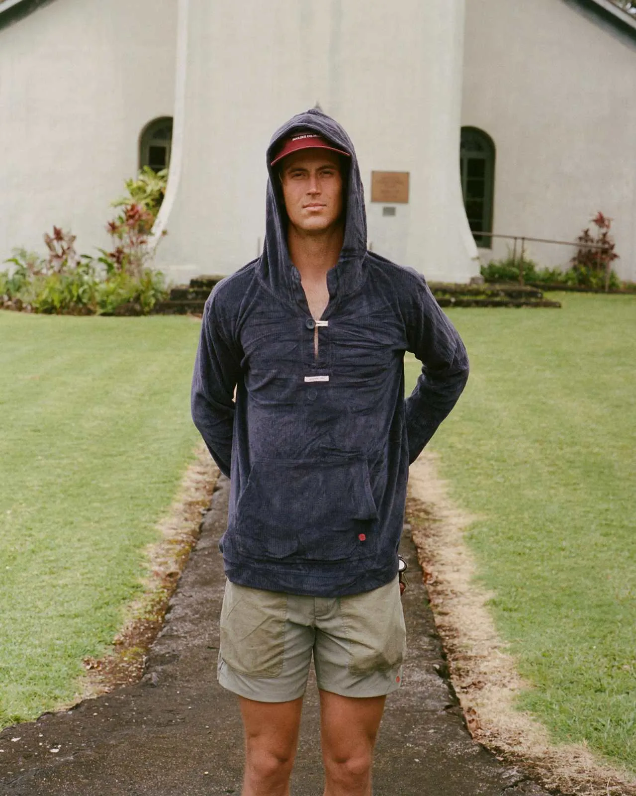 A man wearing a cap and hoodie is standing in front of a building with a lawn.