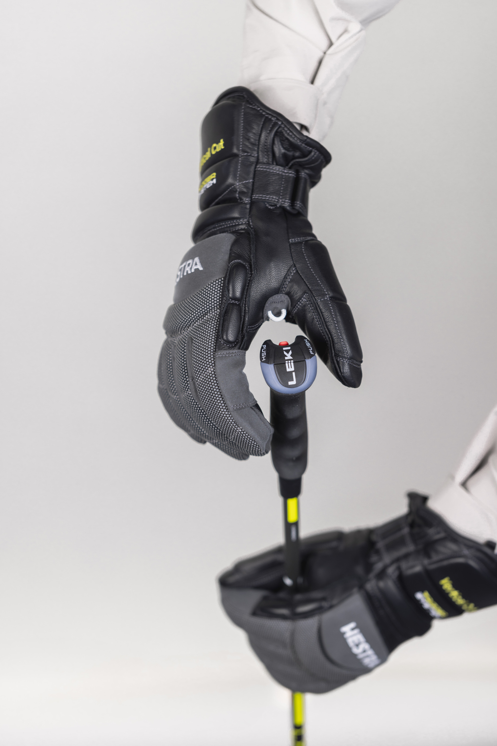 Eine Hand in einem grauen und schwarzen Hestra Skihandschuh hält einen Leki Skistock. Der Handschuh ist mit einem Auslösemechanismus am Stock befestigt.