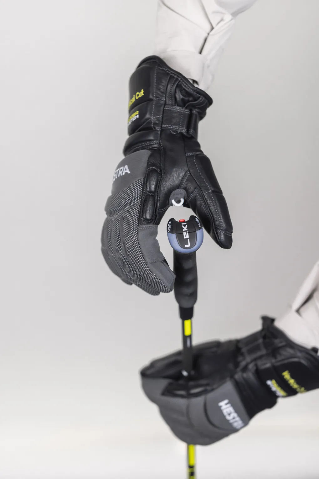 Eine Hand in einem grauen und schwarzen Hestra Skihandschuh hält einen Leki Skistock. Der Handschuh ist mit einem Auslösemechanismus am Stock befestigt.