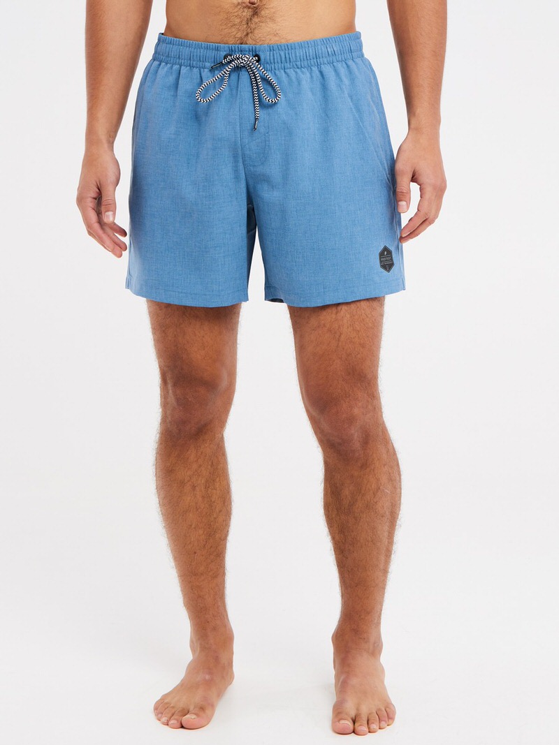 Mann trägt blaue Badeshorts mit Kordelzug und Logo auf hellem Hintergrund.