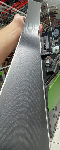 Hand hält einen Ski mit grauer, gewellter Textur vor einem Ski-Geschäft.