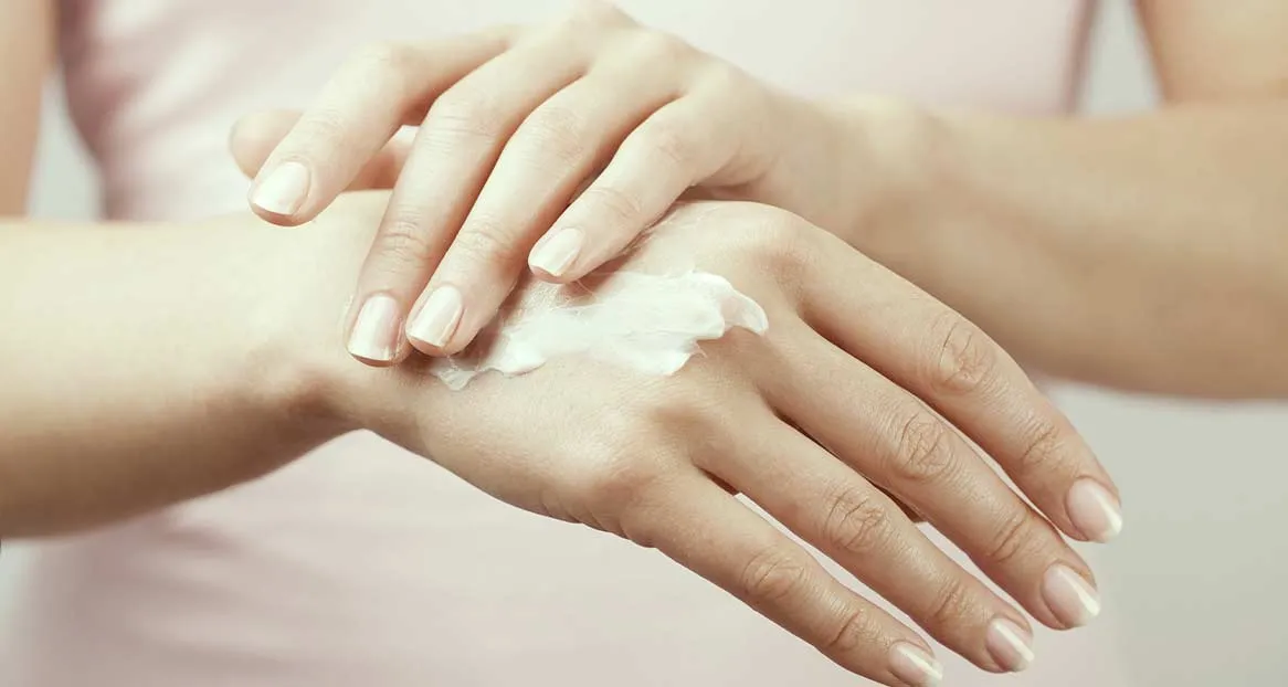 Hände einer Person, die sich Handcreme auf den Handrücken aufträgt. Die Nägel sind gepflegt.