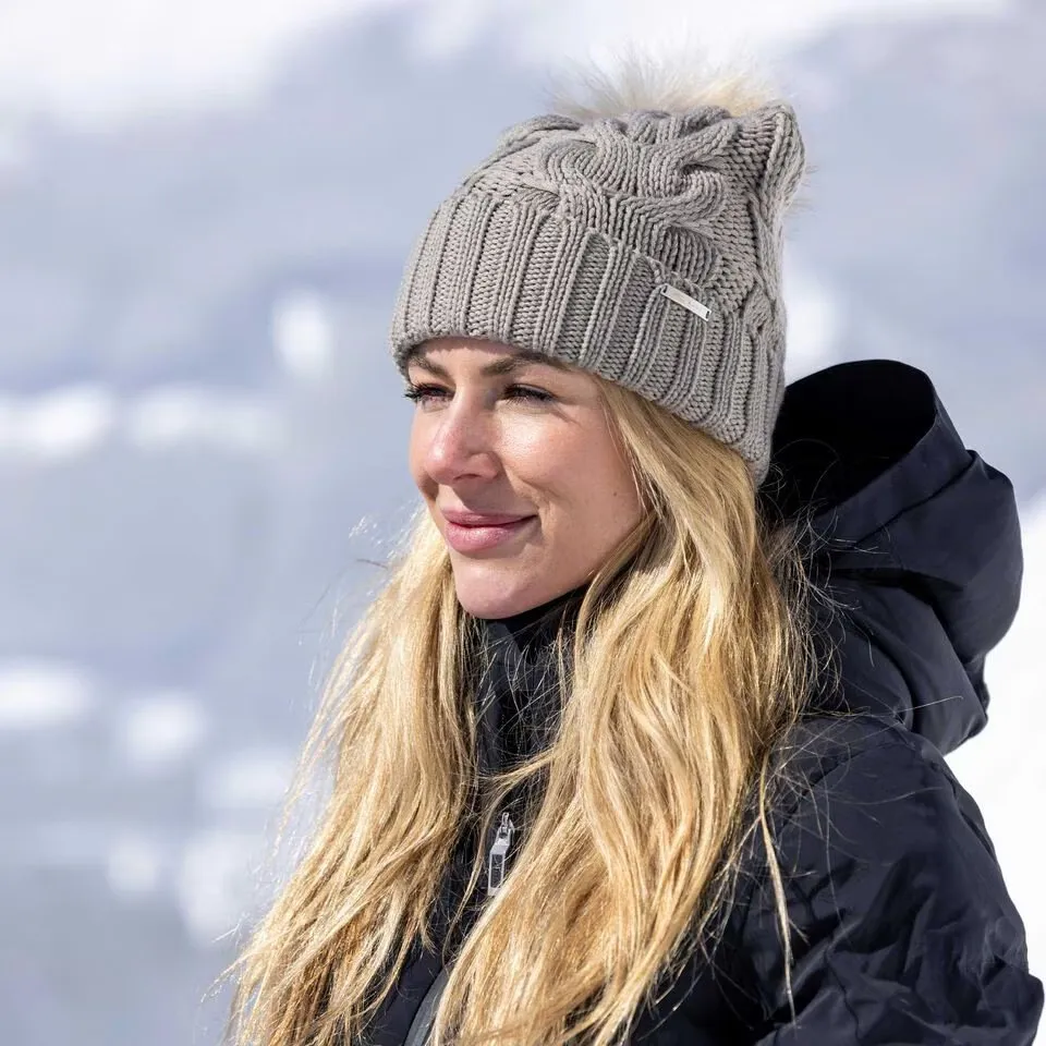 Portrait d'une femme aux cheveux blonds et au bonnet gris tricoté sur fond de neige.