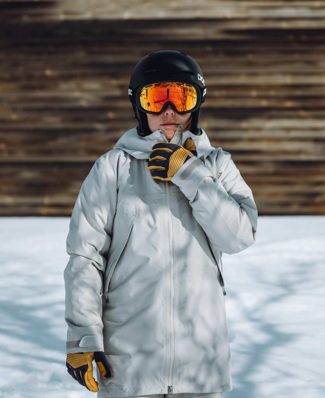 Person mit Fornix Mips Skihelm in Schwarz und orangefarbener Brille, Winterbekleidung und Handschuhen im Schnee.