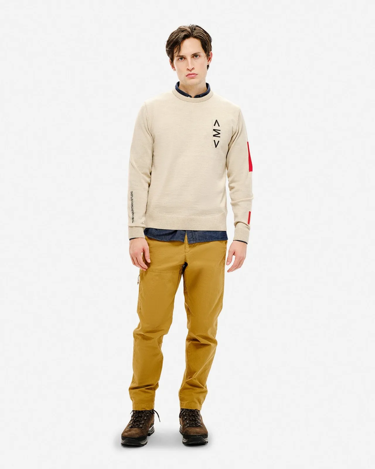 Uomo con maglione da sci beige con motivo, pantaloni e scarpe marroni su sfondo bianco.