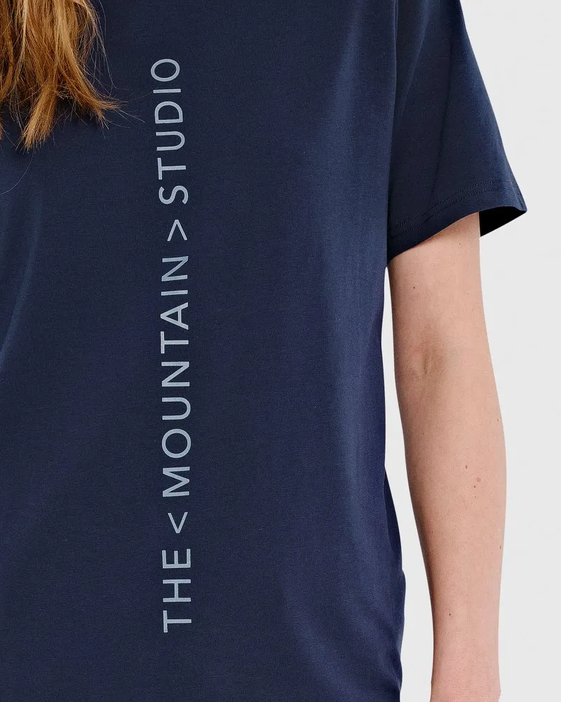 Dark blue T-shirt with vertical, light gray logo print: "THE < MOUNTAIN > STUDIO".