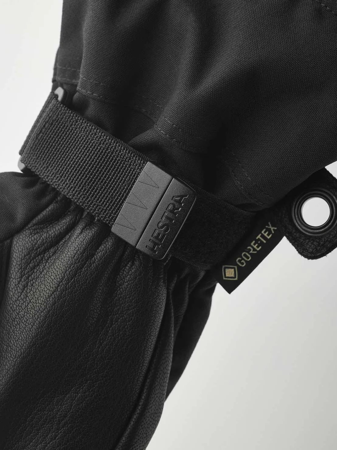 Close-up of a black Hestra glove with Gore-Tex label and adjustable strap. The material is leather and textile.
