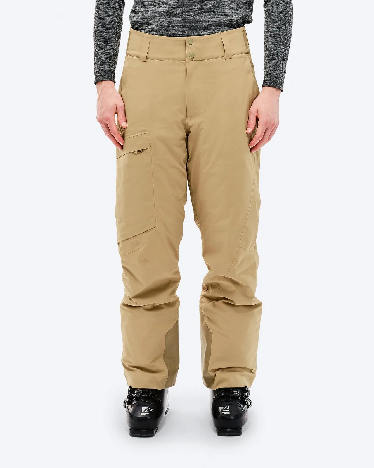 A person wears sand-colored P-1 GORE-TEX 2L Stretch Insulated ski pants and ski boots against a white background.