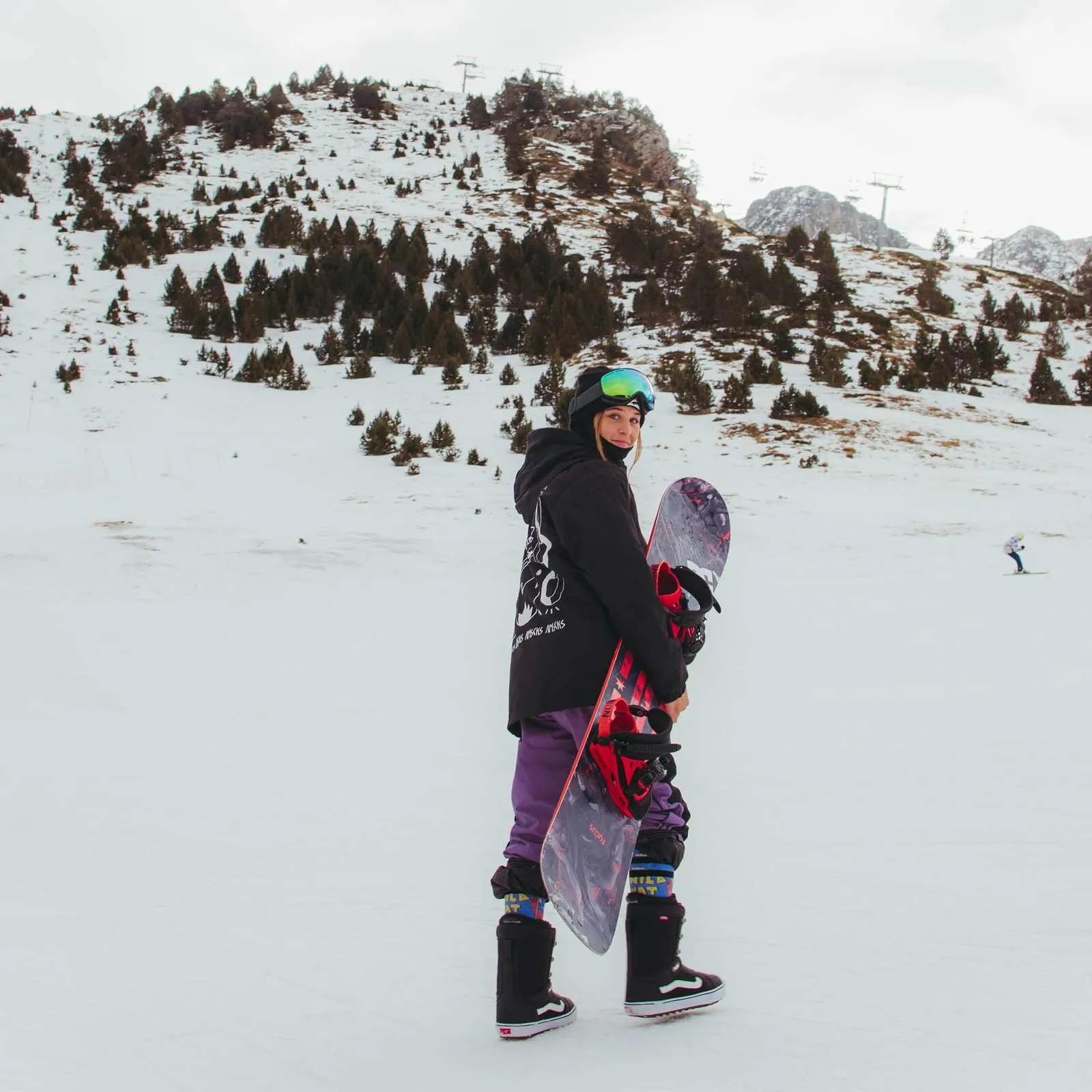 Snowboarder con lo snowboard davanti a un paesaggio montano innevato, con indosso le calze Wild Nature Snow Socks.