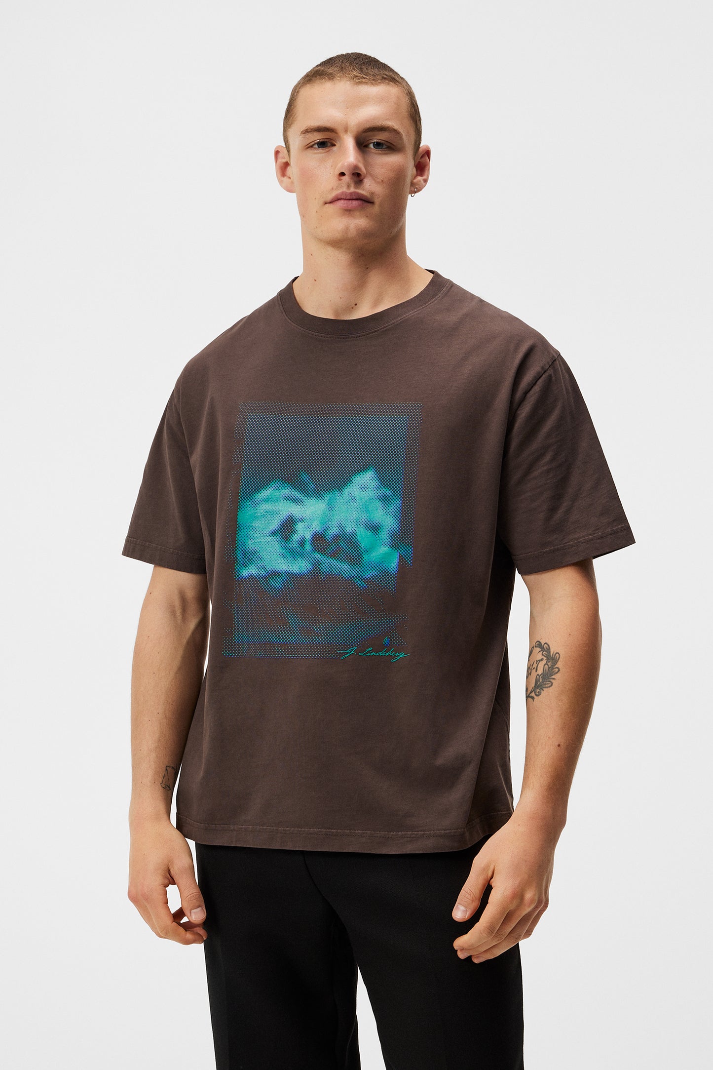 Mann trägt ein braunes T-Shirt mit blauem Print. Das T-Shirt hat eine kastige Passform.