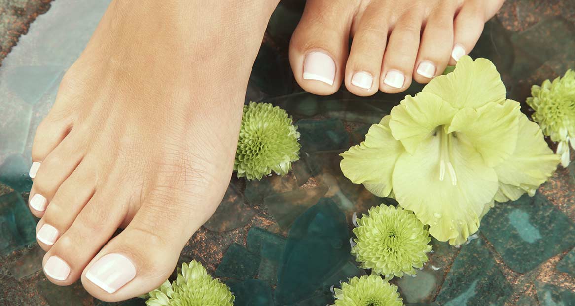 Deux pieds aux ongles d'orteils vernis de couleur claire reposent dans l'eau avec des fleurs vertes. La surface sous l'eau est en forme de mosaïque.